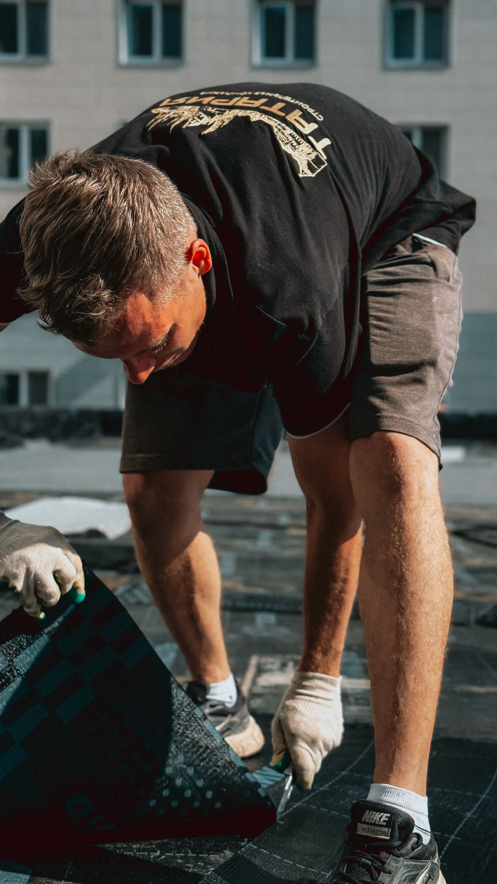Worker applying asphalt shingles on a rooftop under direct sun