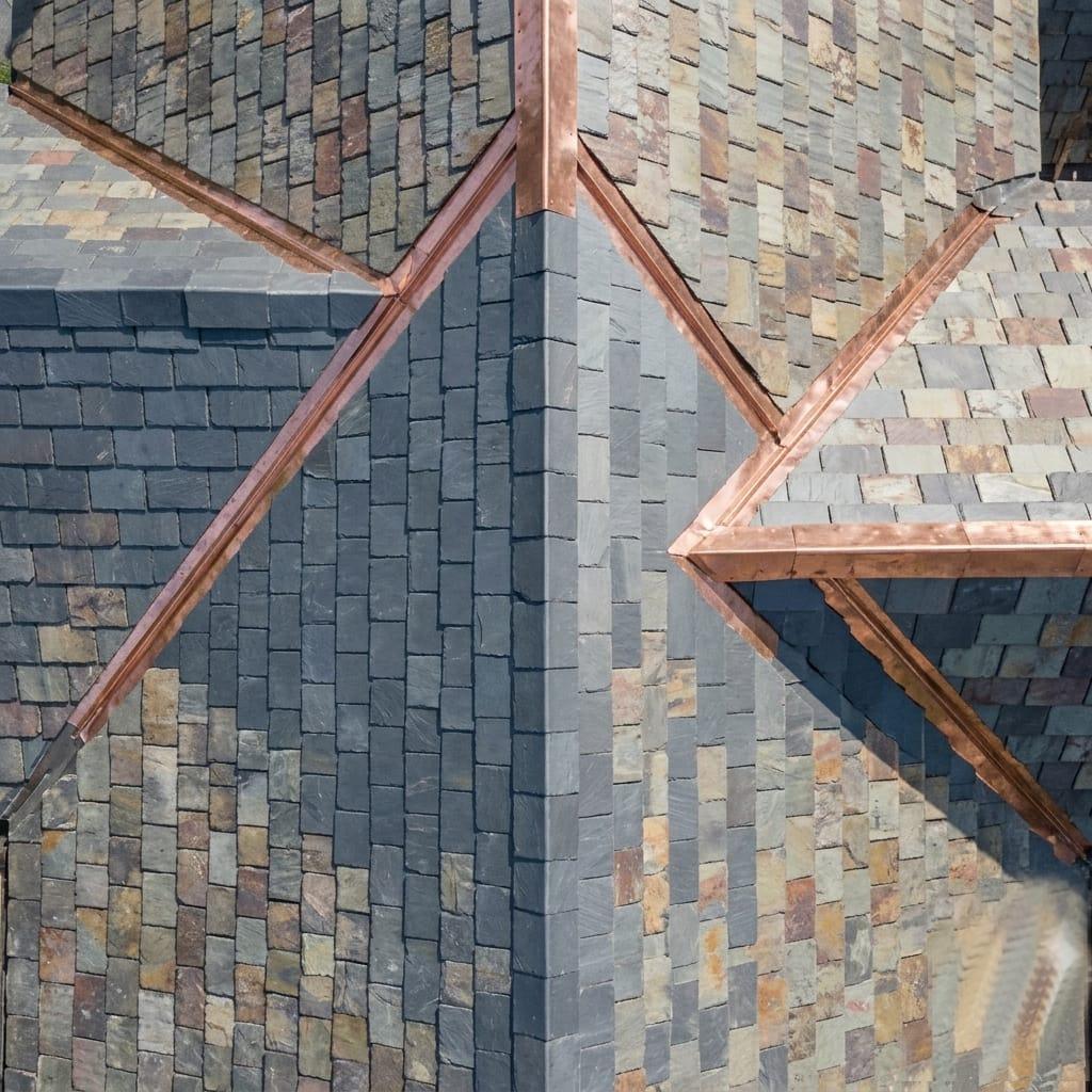 Aerial view showcasing a beautifully crafted roof with varying shades of slate tiles and gleaming copper gutters and flashing. This detailed shot highlights the texture and color variation of the roofing materials. Location: Huntington Beach, United States